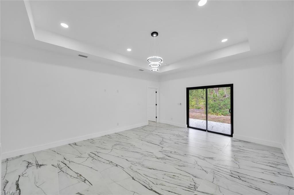 Spacious interior featuring large format marble-look tile flooring, a tray ceiling with recessed lighting, and a modern circular chandelier
