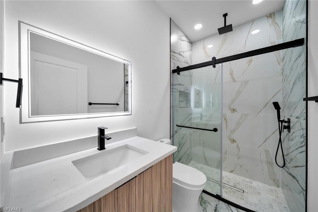 Modern bathroom featuring a back-lit mirror, integrated sink, and wood-finish vanity