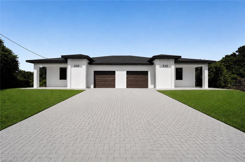 Modern duplex exterior featuring a clean white stucco finish, dark brown garage doors, a black flat roofline, and a herringbone-pattern paver driveway