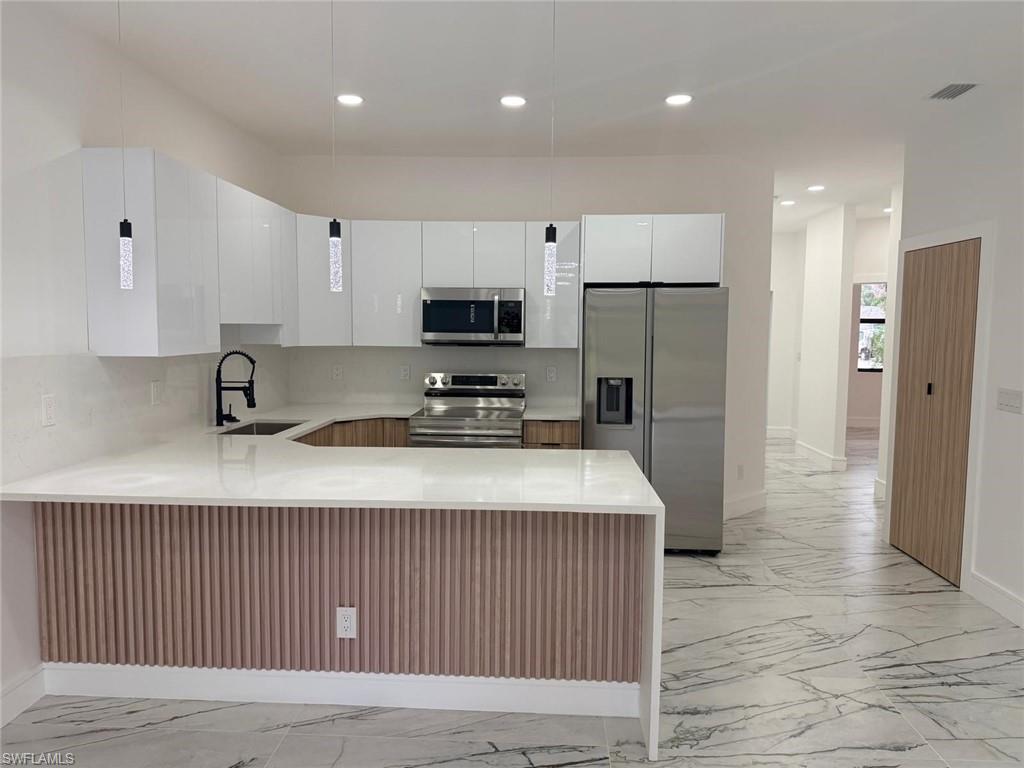 Modern kitchen featuring white glossy cabinetry, stainless steel appliances, a white solid surface countertop, and stylish pendant lighting