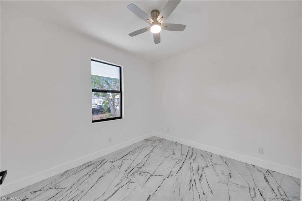 Room featuring large format marble-look tile flooring, a window with black trim, and a ceiling fan with integrated lighting