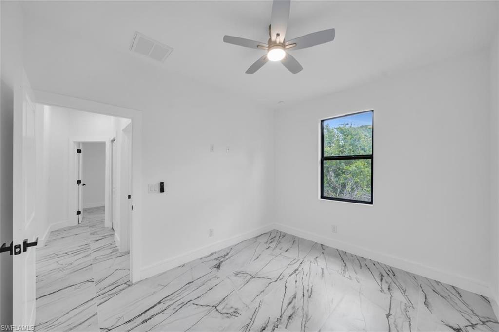 Room featuring large format marble-look tile flooring, a window with black trim, and a ceiling fan with integrated lighting