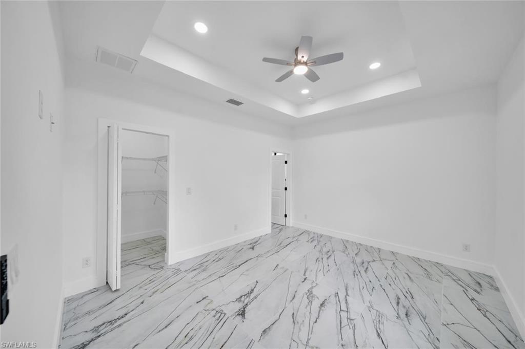 Spacious room featuring large format tile flooring, a tray ceiling with recessed lighting, and a ceiling fan