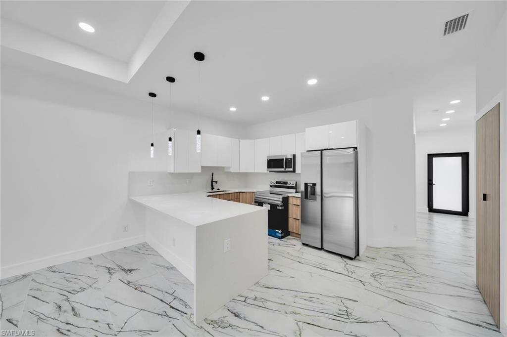 Modern kitchen featuring white cabinetry, light wood-finish lower cabinets, stainless steel appliances, and a solid surface countertop with an integrated breakfast bar