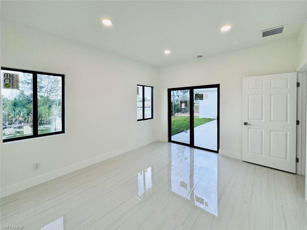 Spacious room featuring white tile flooring, recessed lighting, white walls, black-framed windows, and sliding glass doors opening to the exterior