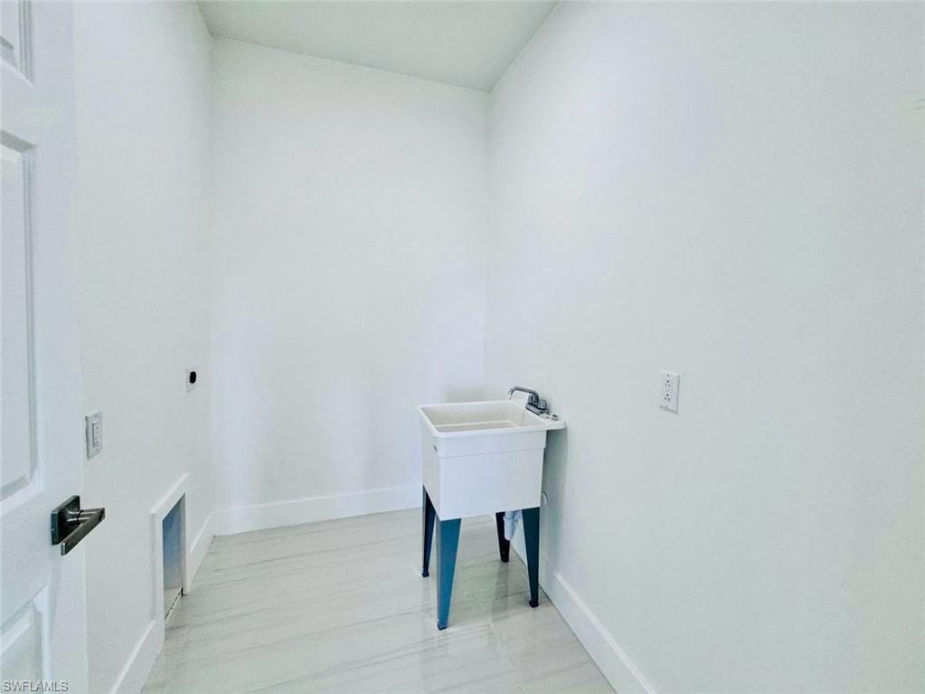 Utility room featuring a laundry basin with a single-handle faucet, light-toned tile flooring, white baseboards, and a white paneled door with dark hardware