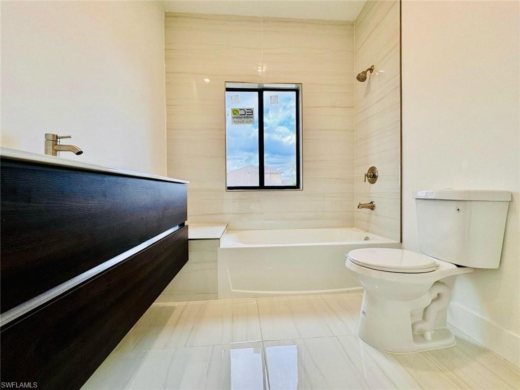Bathroom featuring a floating dark wood-finish vanity with a white countertop and brushed nickel faucet, a white bathtub, a window with a dark frame, and light-toned tile flooring and wall surround