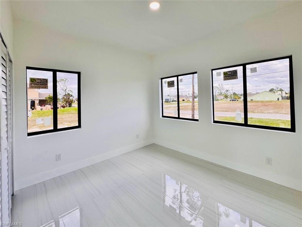 Bright room featuring three windows with black frames, white walls, white baseboards, and polished tile flooring with a subtle veining pattern