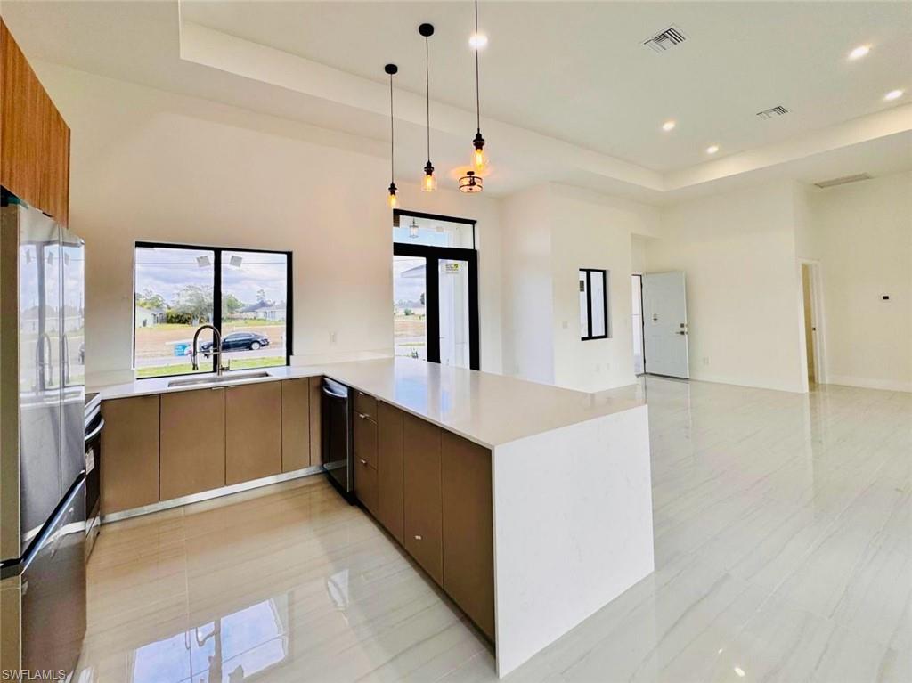 Contemporary kitchen featuring a large waterfall island with a quartz countertop, sleek cabinetry, stainless steel appliances, and a built-in sink under a window