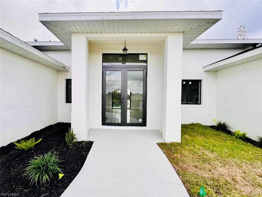 Contemporary architecture featuring a grand double-door entry with dark frames, a covered portico, and a concrete pathway