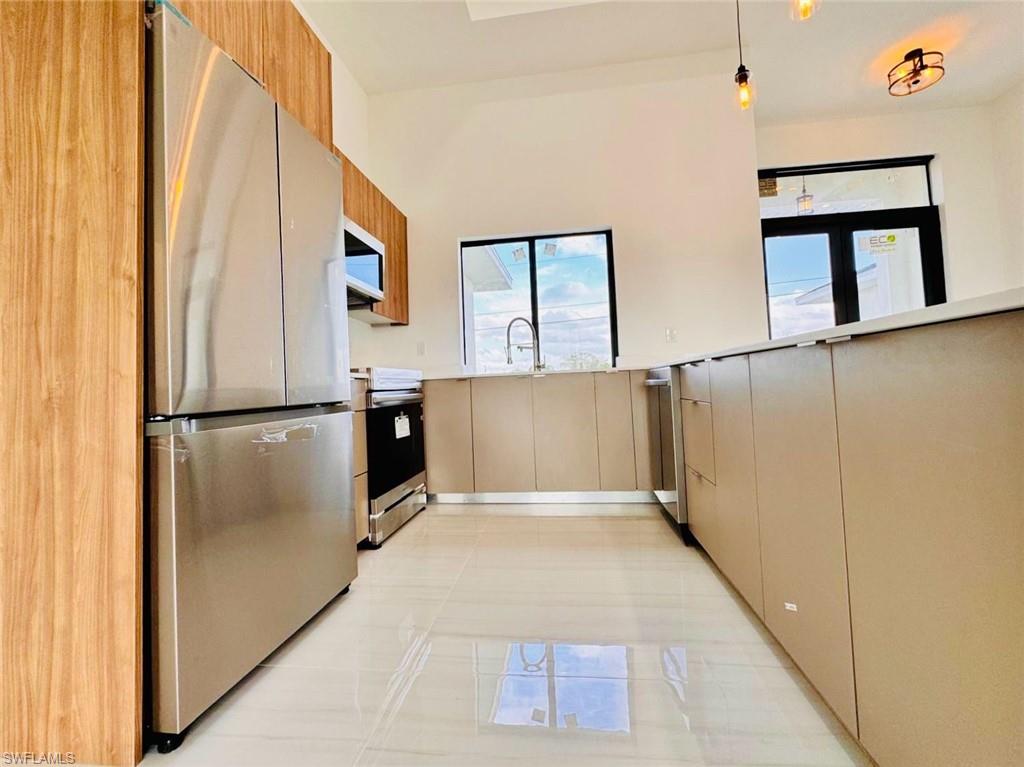 Modern kitchen featuring stainless steel appliances, wood-finish cabinetry, light-toned flat-panel lower cabinets, light countertops, and polished tile flooring