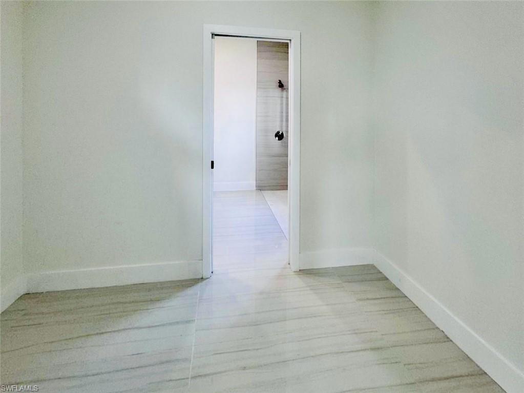 Light-toned walls with crisp white baseboards and a doorway framing a secondary space featuring a shower with dark fixtures