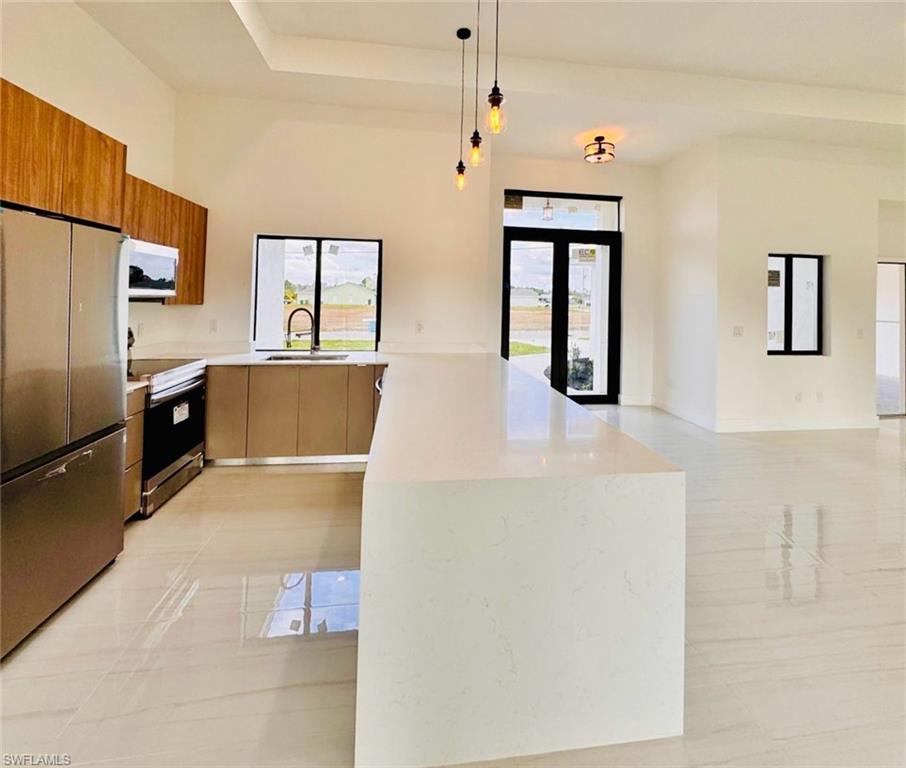 Contemporary kitchen featuring a waterfall island with a light-toned countertop, stainless steel appliances, and wood-finish upper cabinetry