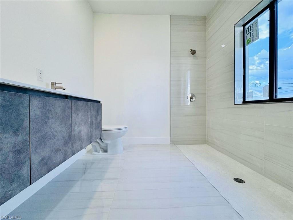 Sleek modern bathroom featuring large format tile flooring, a floating vanity with a light-toned countertop, a contemporary wall-mounted faucet, a curbless shower with a linear drain, and a black-framed window
