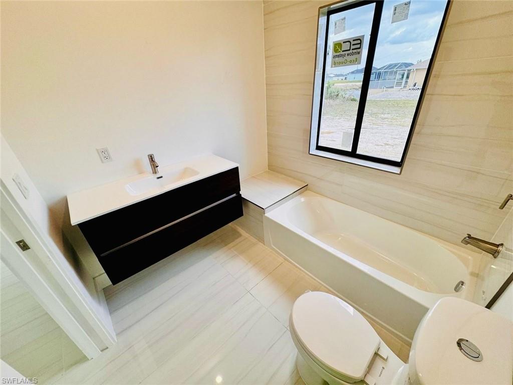 Bathroom featuring a floating vanity with integrated sink, a white bathtub, and a window with black trim