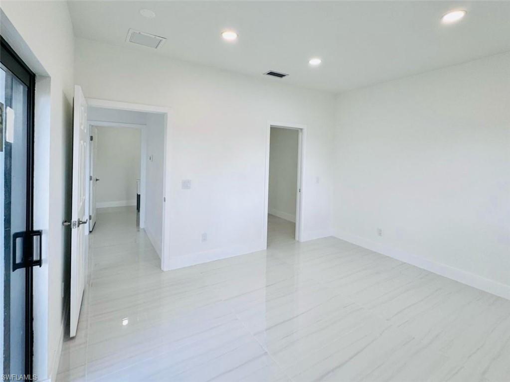 Spacious interior room featuring light-colored tile flooring, white walls, and recessed lighting