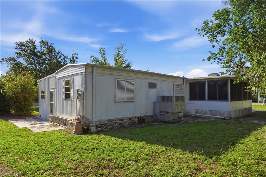 Exterior featuring white corrugated siding, a screened enclosure, a concrete patio, and mature trees surrounding the property