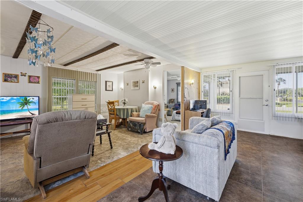 Spacious interior featuring a combination of wood-finish and tile flooring, vertical window blinds, a built-in ceiling fan, and exposed ceiling beams