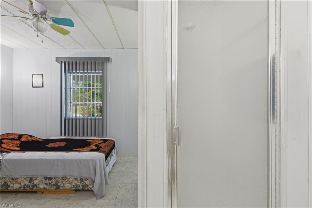 Room with paneled walls, a window featuring vertical blinds, and a ceiling fan