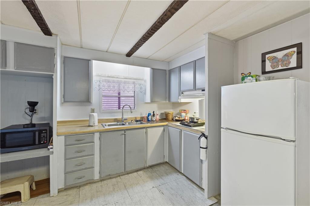 Kitchen featuring light gray cabinetry, wood-finish countertops, stainless steel sink, and white appliances
