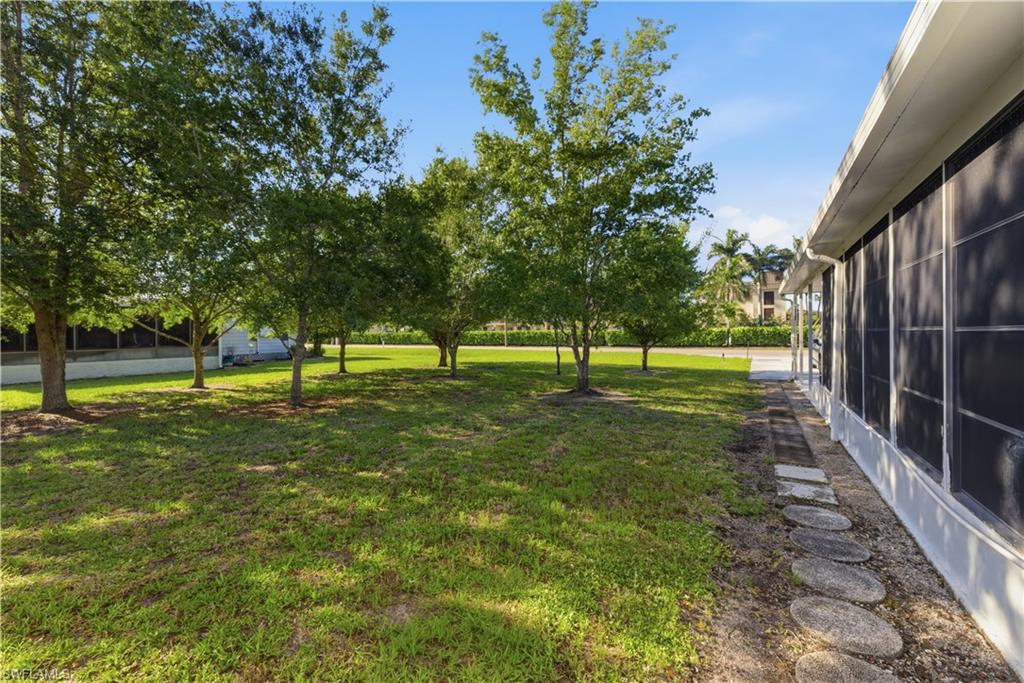 Expansive side yard featuring mature trees and a stone paver pathway bordering the screened enclosure
