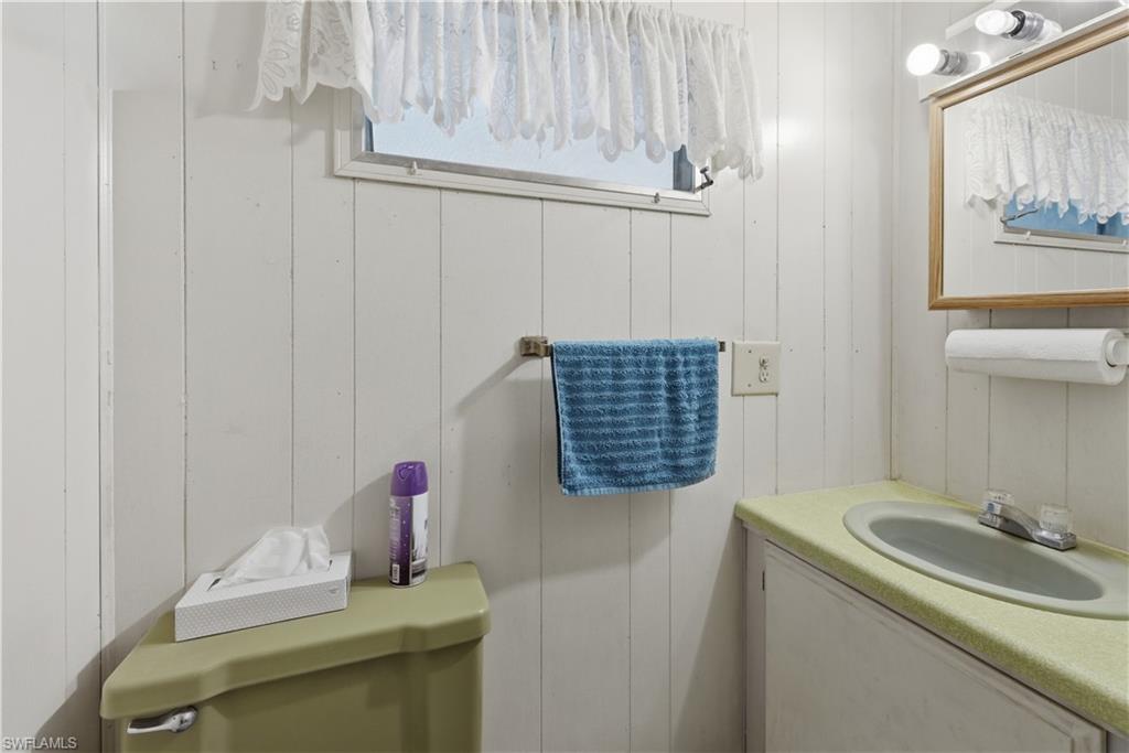 Bathroom featuring vertical paneled walls, a single window with curtain, an oval sink with a laminate countertop, and a wall-mounted mirror