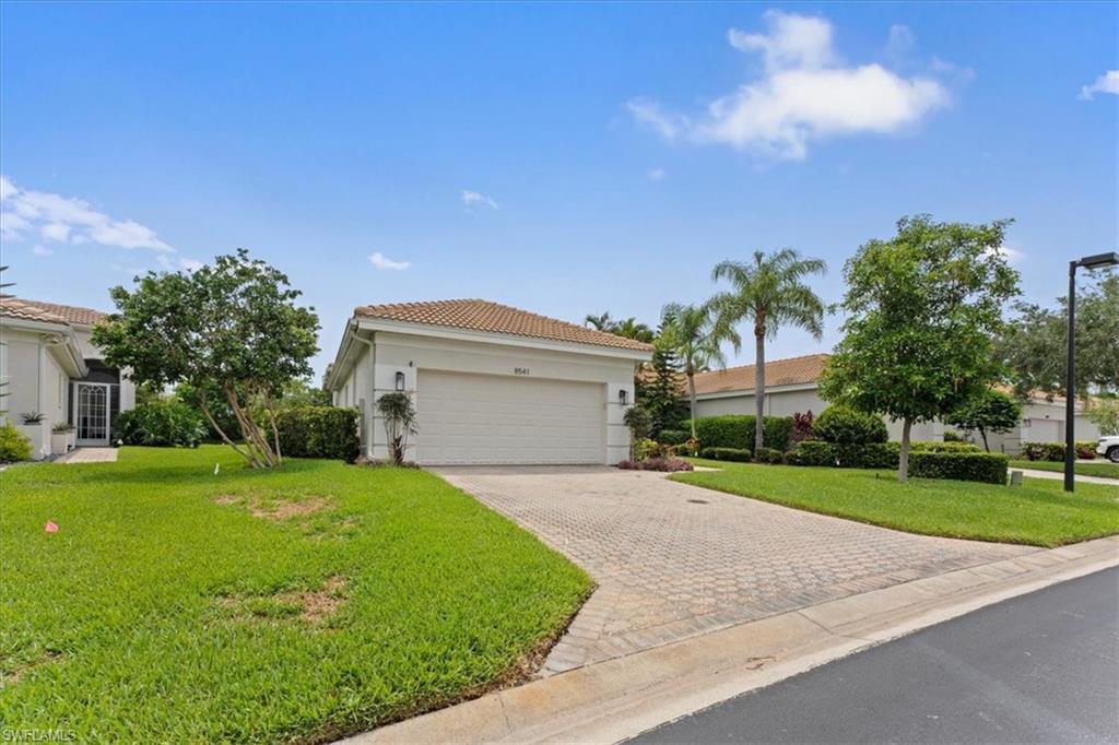 View of front of property featuring a garage, decorative driveway, stucco siding, and a front lawn