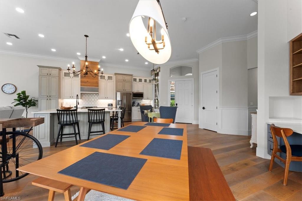 Dining area featuring a chandelier, wood finished floors, crown molding, recessed lighting, and a wainscoted wall