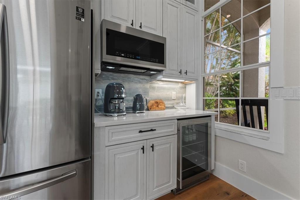 Indoor bar featuring stainless steel appliances, beverage cooler, backsplash, dark wood-type flooring, and baseboards