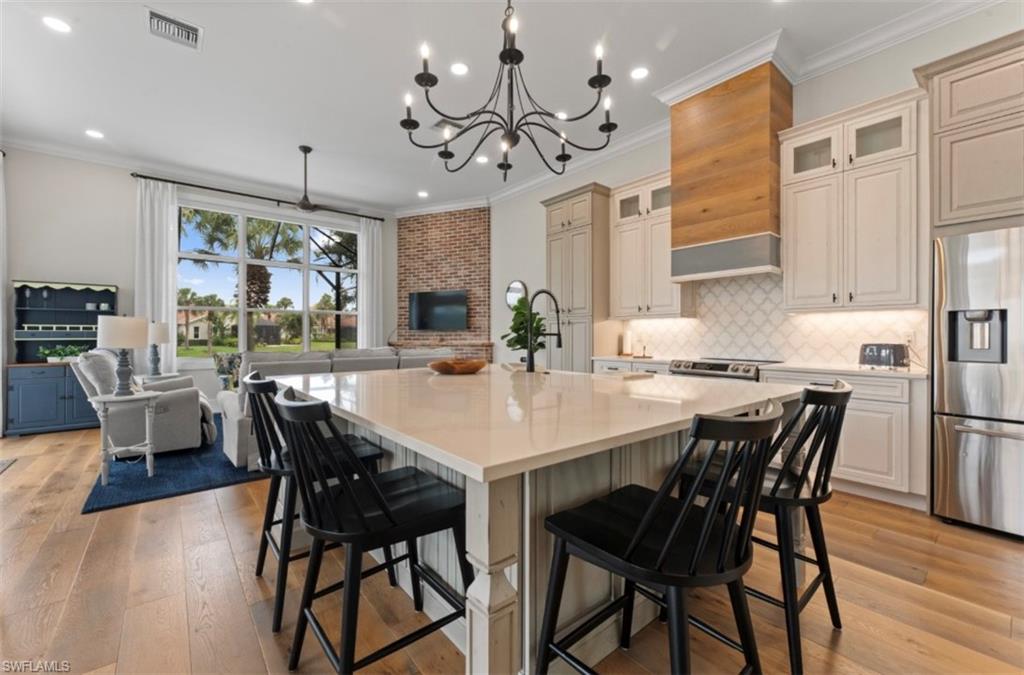 Kitchen with appliances with stainless steel finishes, a kitchen island with sink, light countertops, crown molding, and light wood-type flooring