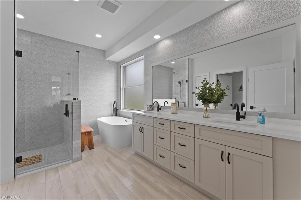 Bathroom featuring a stall shower, double vanity, a freestanding bath, wood finished floors, and recessed lighting