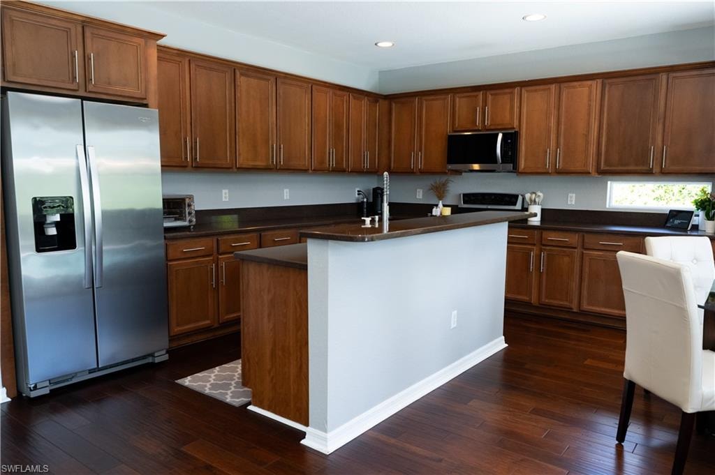 Kitchen featuring rich wood-finish flooring, ample cabinetry with brushed nickel hardware, dark countertops, a stainless steel refrigerator, and recessed lighting