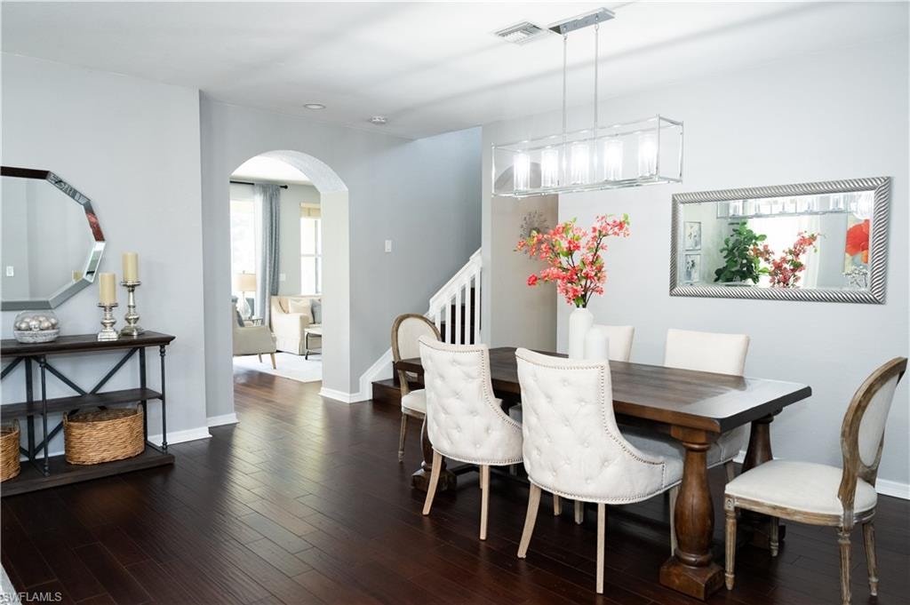 Spacious dining area featuring dark wood-finish flooring, a contemporary linear chandelier, an arched entryway, and a staircase with white balusters
