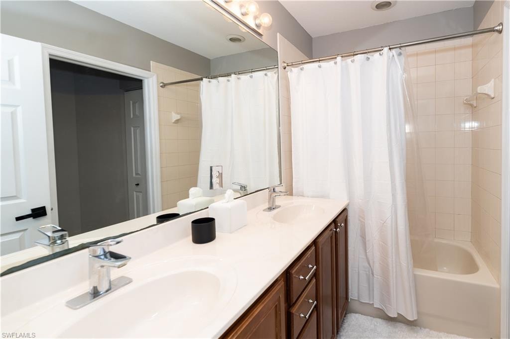 Bathroom featuring a double vanity with integrated sinks, a wide mirror, and a full-size bathtub with a tile surround