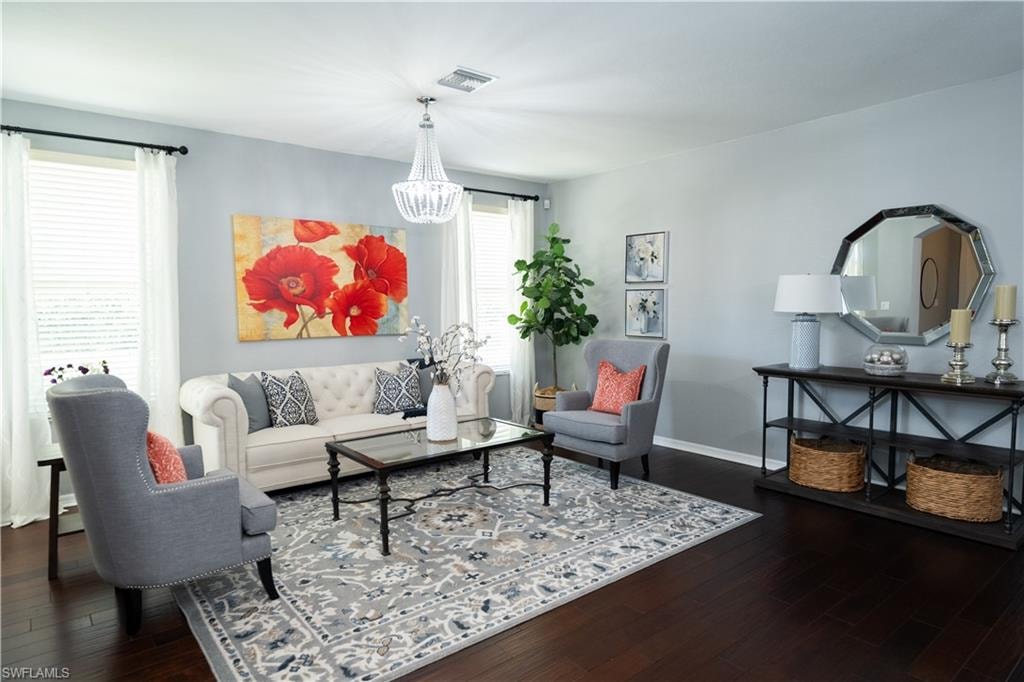 Open-concept living space featuring rich wood-finish flooring, a contemporary chandelier, ample natural light from multiple windows, and a built-in console table with shelving
