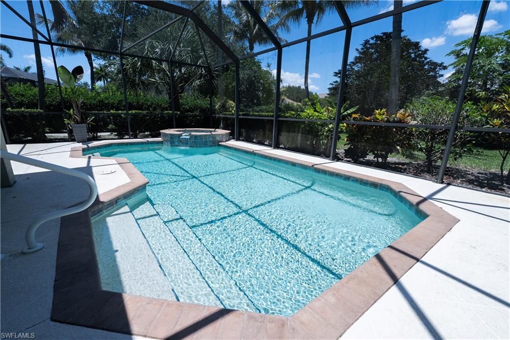 Screened swimming pool featuring a built-in spa with a waterfall, ample deck space, and integrated steps