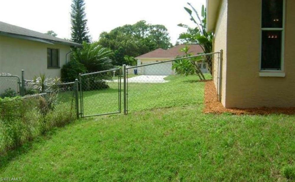 Grassy yard space featuring a chain-link fence with gate and mature landscaping