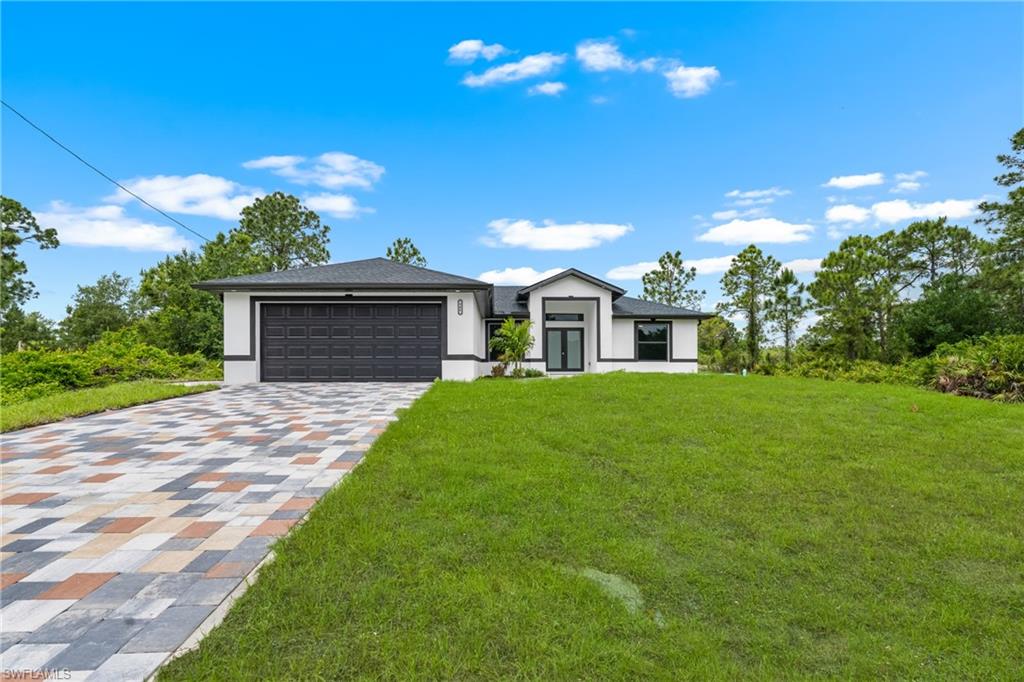 Modern single-story residence featuring a dark gray garage door and a multicolored paver driveway