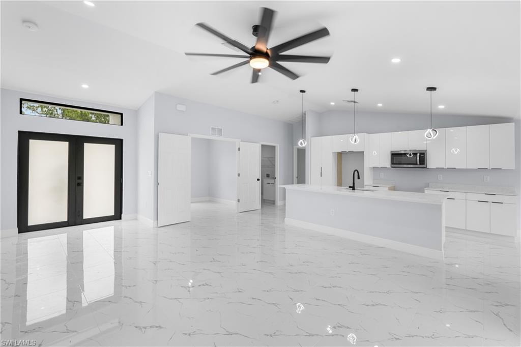 Open-concept living space featuring high ceilings, large format tile flooring, a modern kitchen with a center island and pendant lighting, and double entry doors with an overhead transom window