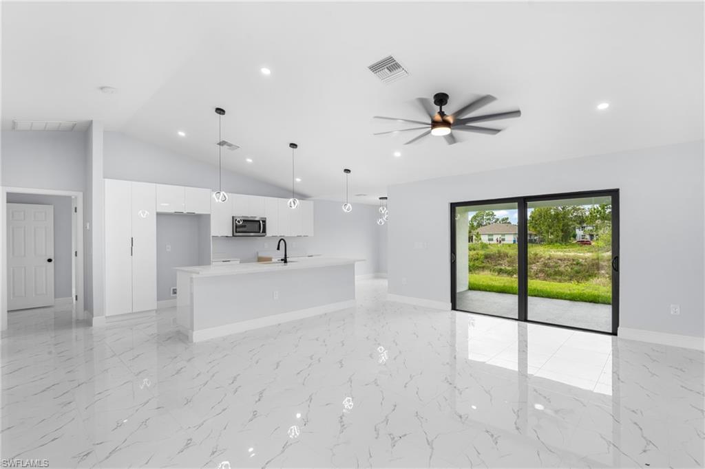 Open-concept living space featuring high vaulted ceilings, modern kitchen cabinetry, sleek tile flooring, a large kitchen island, and sliding glass doors to the outdoor patio
