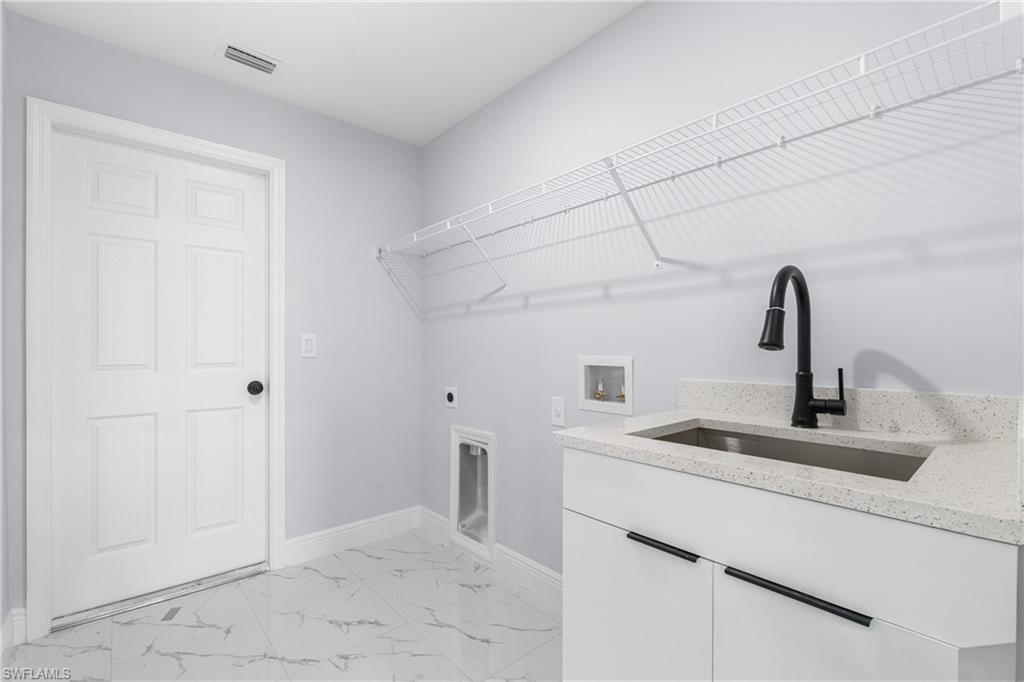 Utility room featuring white cabinetry, a light-toned countertop, an undermount sink with a black faucet, and white wire shelving
