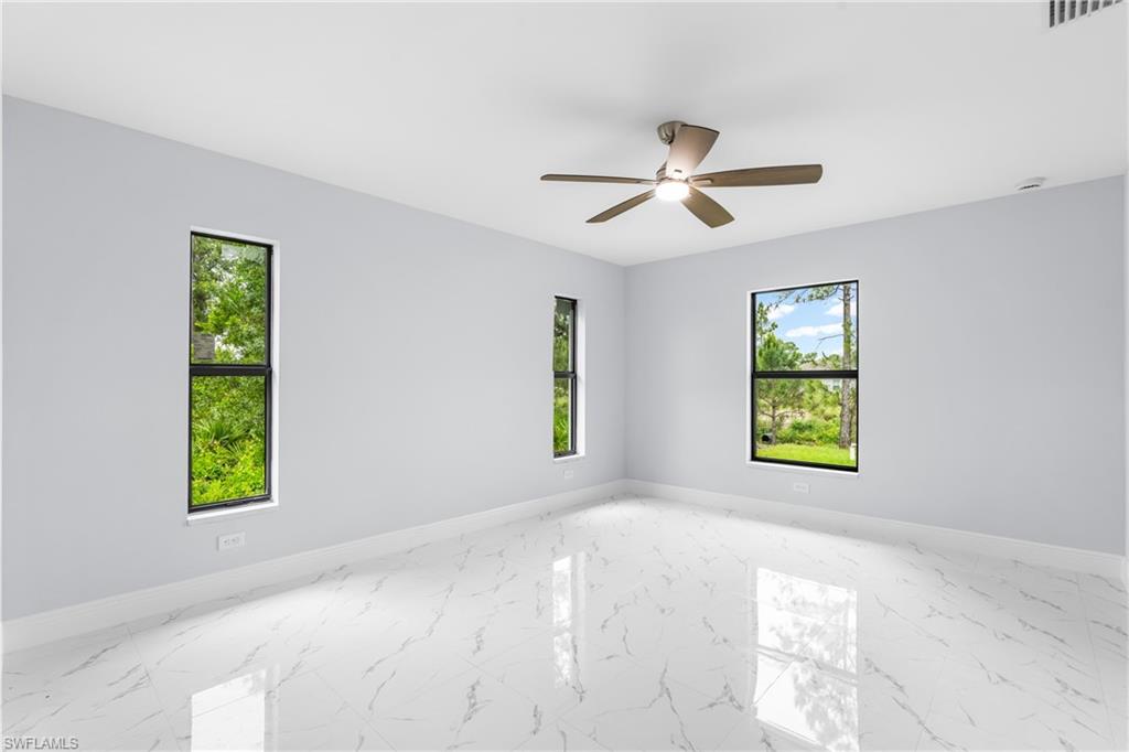 Spacious interior featuring reflective tile flooring, multiple windows providing abundant illumination, and a ceiling fan with integrated lighting