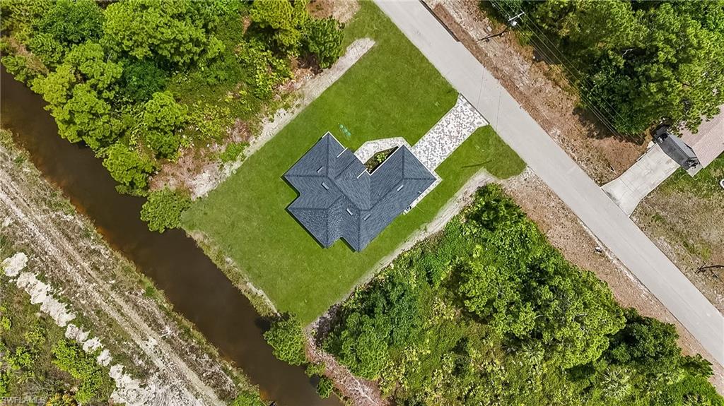 Aerial overview showcasing a property with a dark shingle roof, a light-colored paved driveway, and a manicured green lawn
