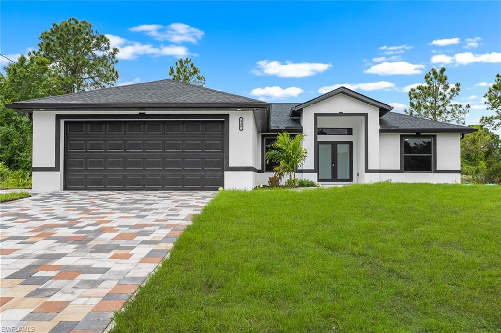Contemporary exterior featuring a textured stucco finish with dark trim accents, a large two-car garage, a patterned paver driveway, an architectural shingle roof, and an inviting double-door entry with transom window