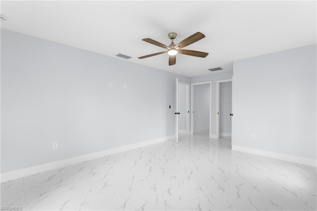 Spacious room featuring white large format tile flooring, light blue walls, and a wood-finish ceiling fan with integrated lighting