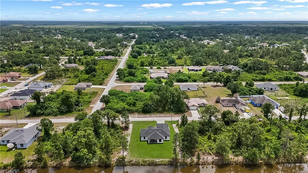 Aerial perspective showcasing a single-story residence with a dark roof against a backdrop of abundant green landscaping
