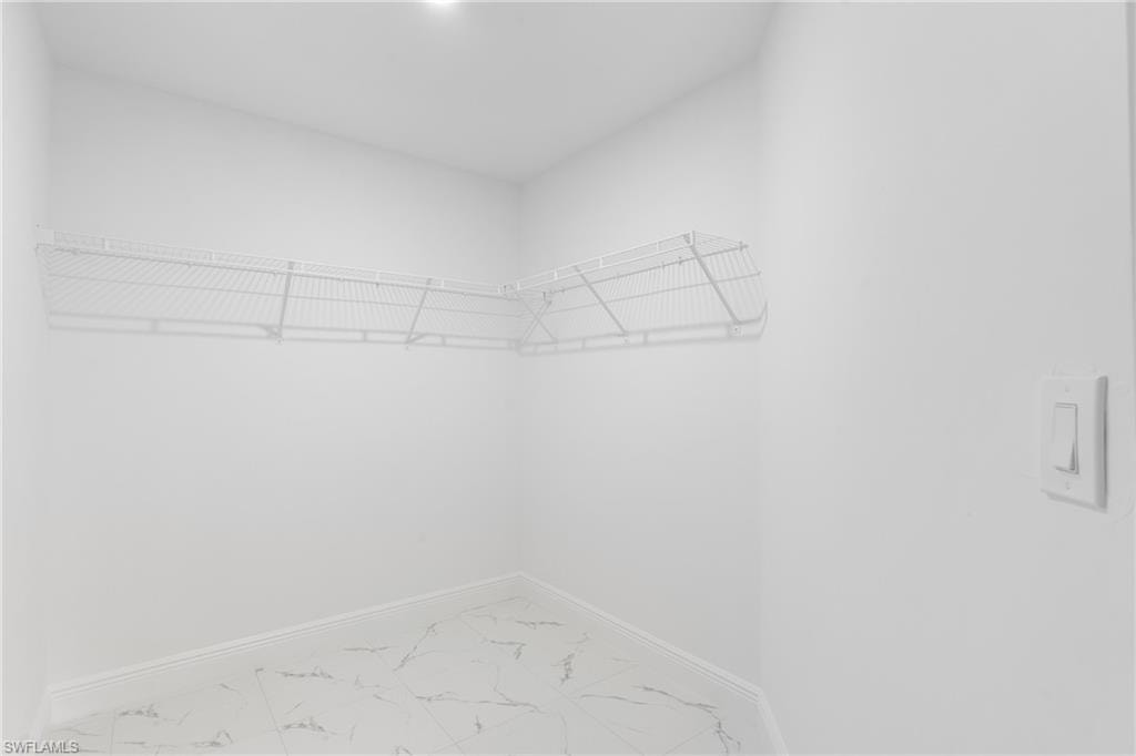 Corner closet space featuring wire shelving, white baseboards, and marble-look tile flooring