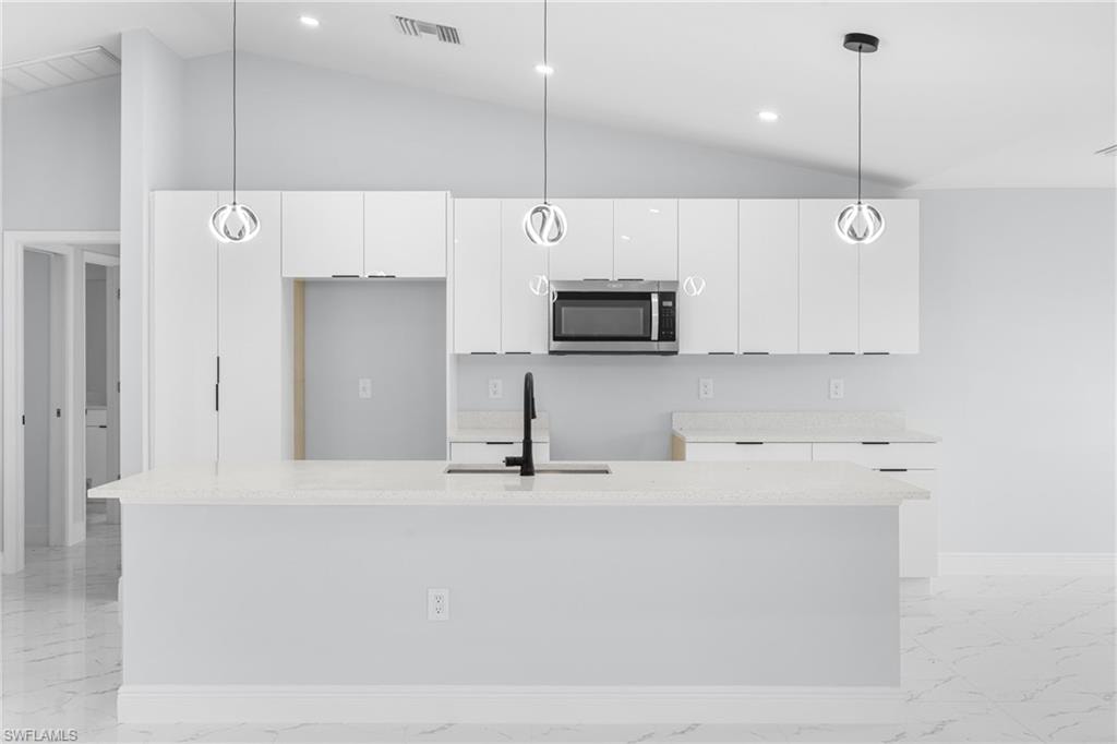 Contemporary kitchen featuring an expansive island with a light-toned countertop, white glossy cabinetry, stainless steel microwave, and three pendant light fixtures