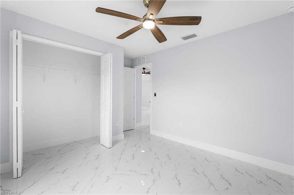 Spacious room featuring large format tile flooring, a ceiling fan with wood-finish blades, light-toned wall paint, and bi-fold closet doors with built-in shelving