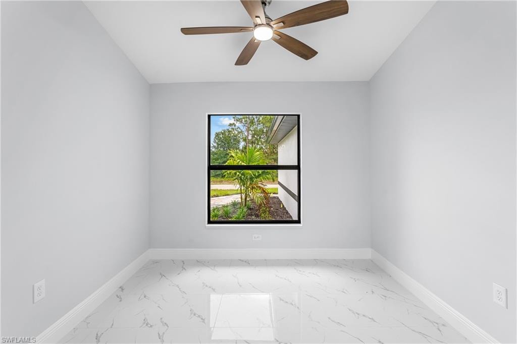 Bright interior space featuring a window with black trim, a ceiling fan with wood-finish blades, pristine white walls, and a white marble-look tile floor